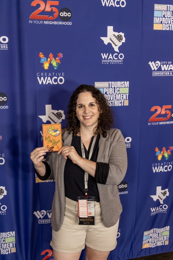 Chen Drachman on the red carpet at the 2025 Waco Independent Film Festival, holding a postcard of her film "But I'm a Shoe"
